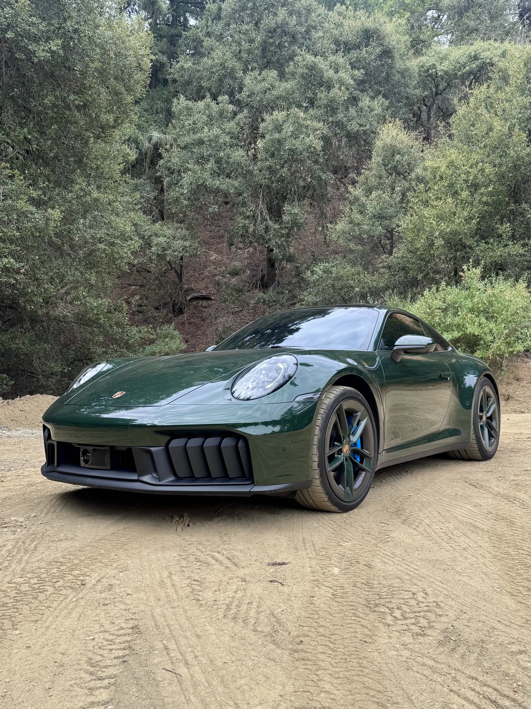Oak green Porsche 911 Carrera 4 GTS parked on a dirt pull-out below a hillside of fir and oak